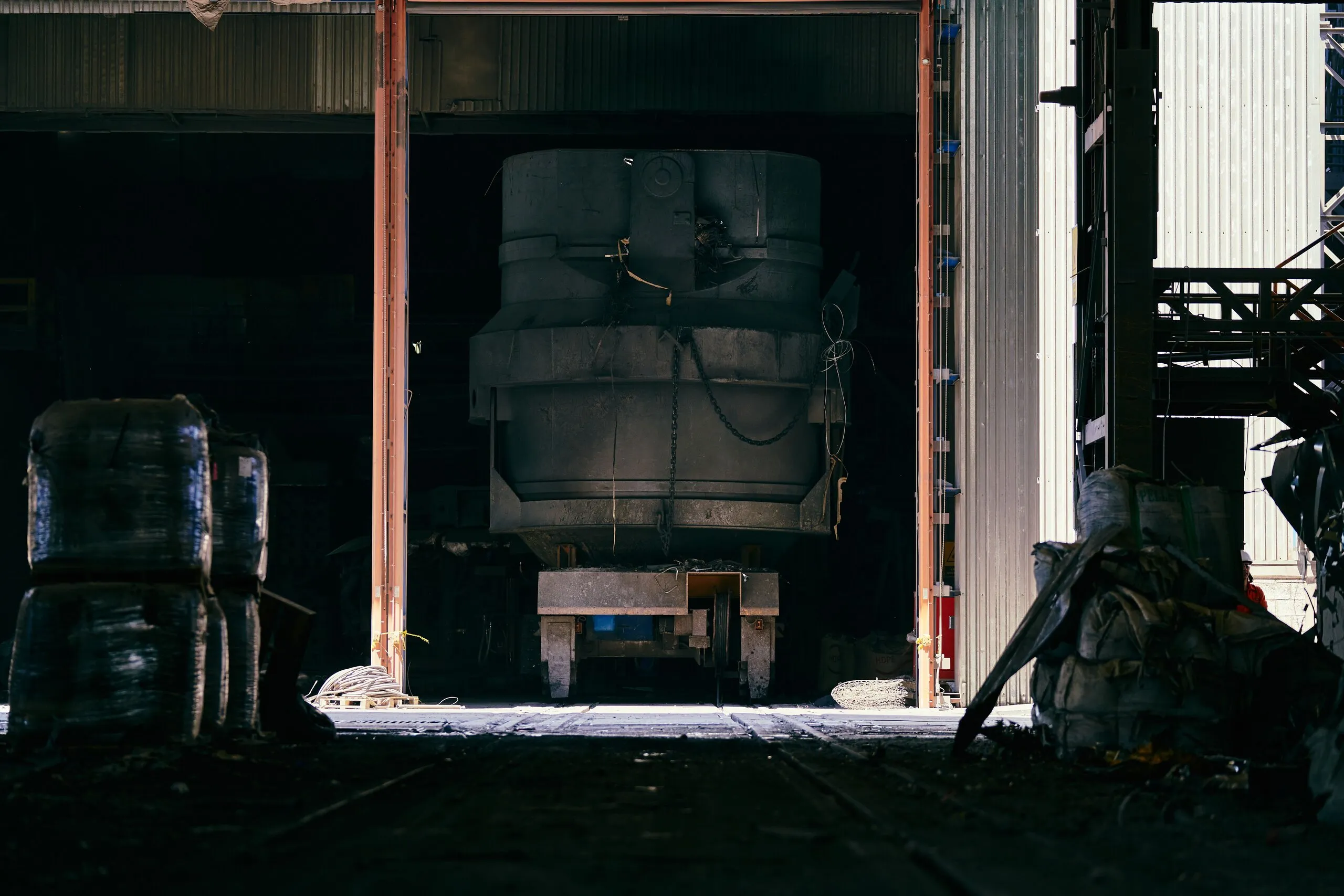 A steel ladle standing in the doorway of a refractory works, a worker beside it