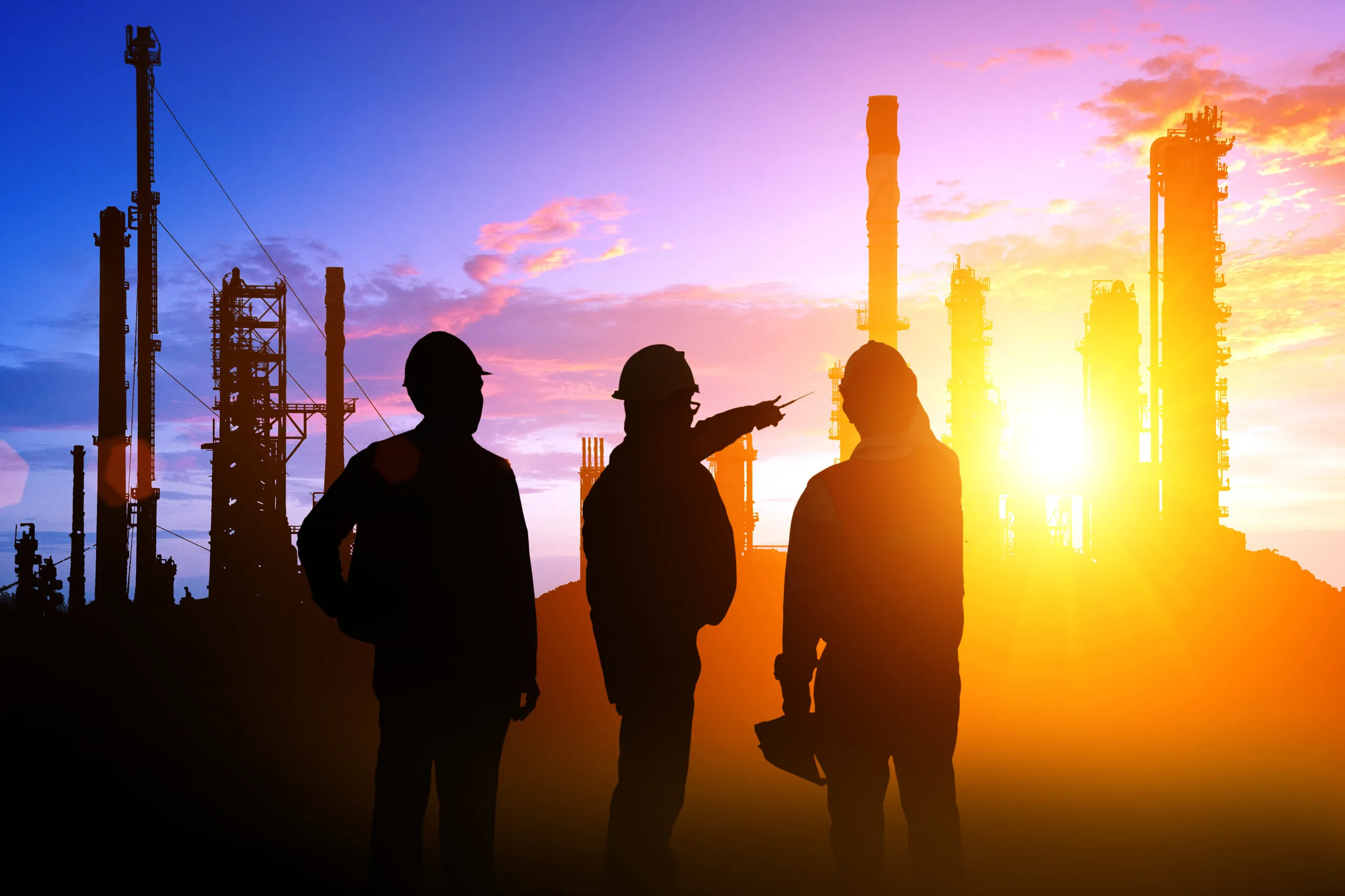 Three workers in hard hats silhouetted against a sunset